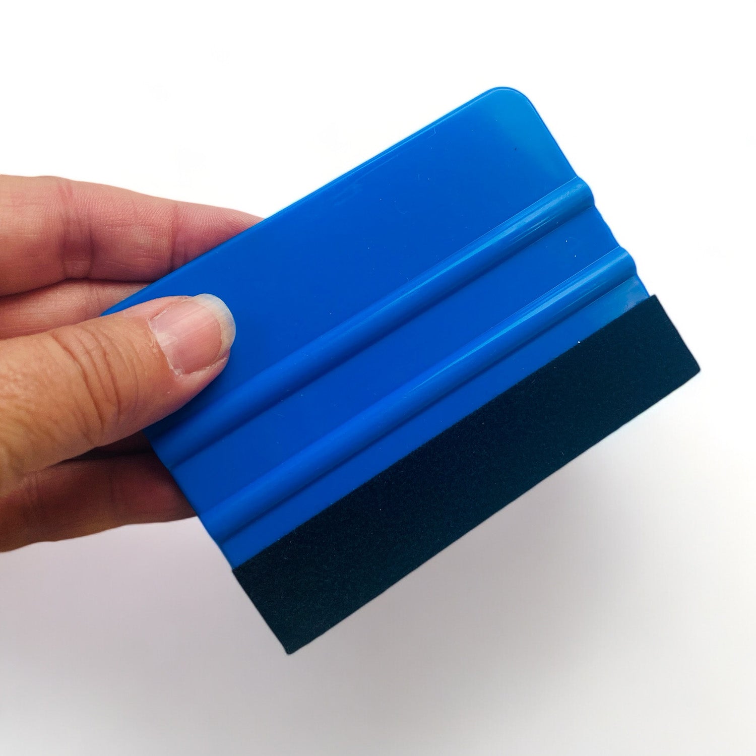 A hand is shown holding a 4 inch rectangular blue handled felt edge crafting squeegee against a white background.