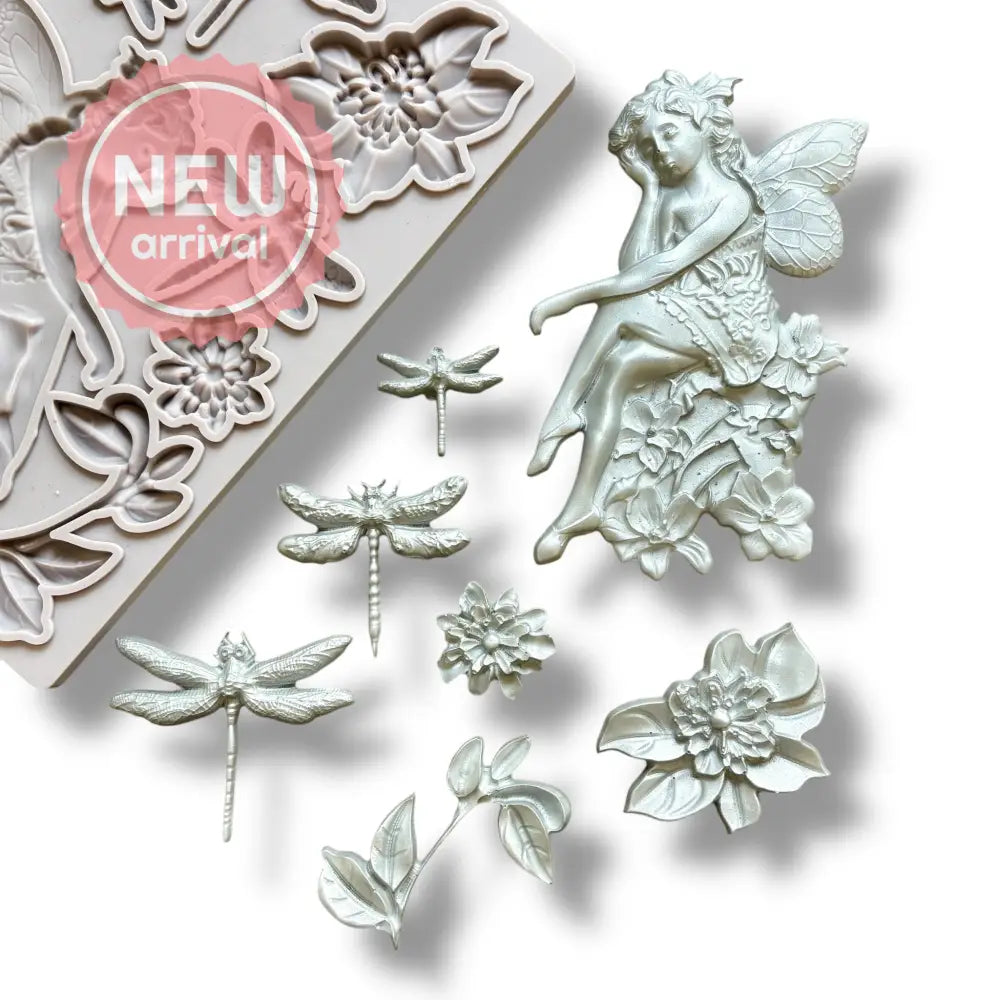 A light grey silicone mold and silver colored castings of a fairy sitting on a cluster of flowers, 2 single flowers, leaves, and 3 dragonflies are against a white background.