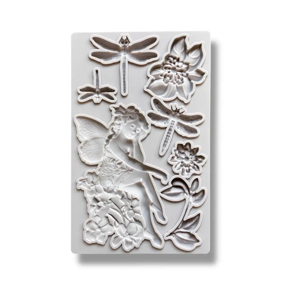 A light grey silicone mold featuring a fairy sitting on a cluster of flowers, 2 single flowers, leaves, and 3 dragonflies is against a white background.