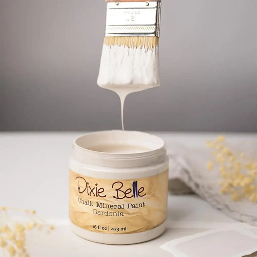 A paint brush with dripping paint is shown above an open container of Dixie Belle's Gardenia Chalk Mineral Paint.