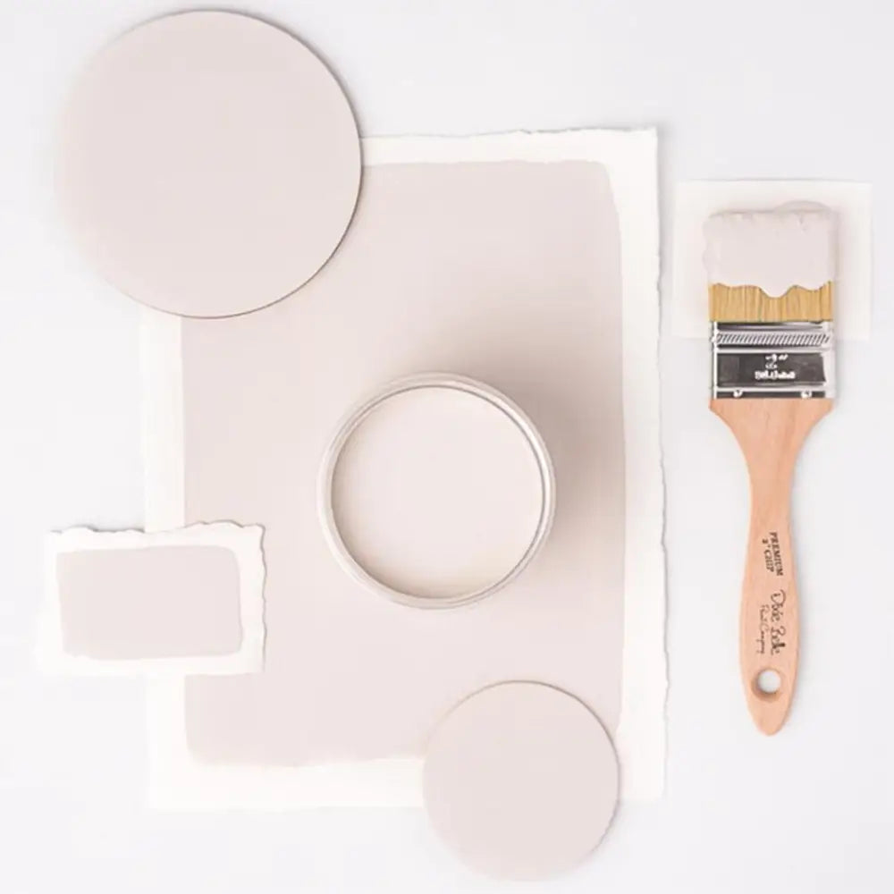 A paint brush, paper, and round wood samples of Dixie Belle's Gardenia Chalk Mineral Paint are against a white background.