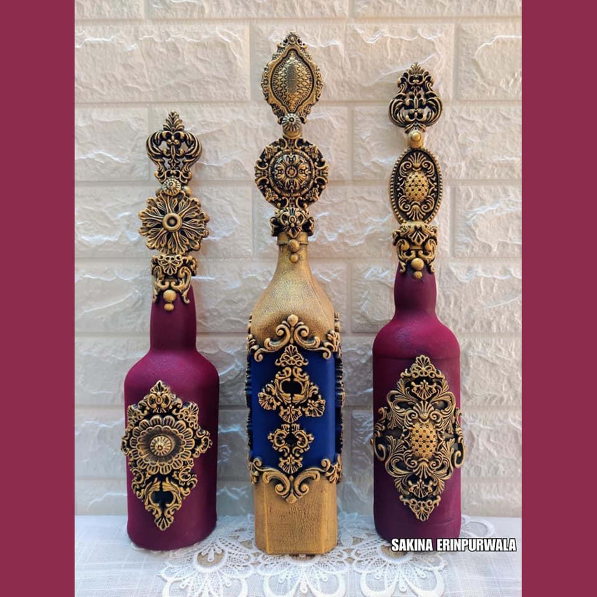 Two royal purple, and 1 gold and royal blue glass bottles feature Dadarkar Art by Get Inspired's Crowns of Bavaria silicone mold castings painted in gold on them.