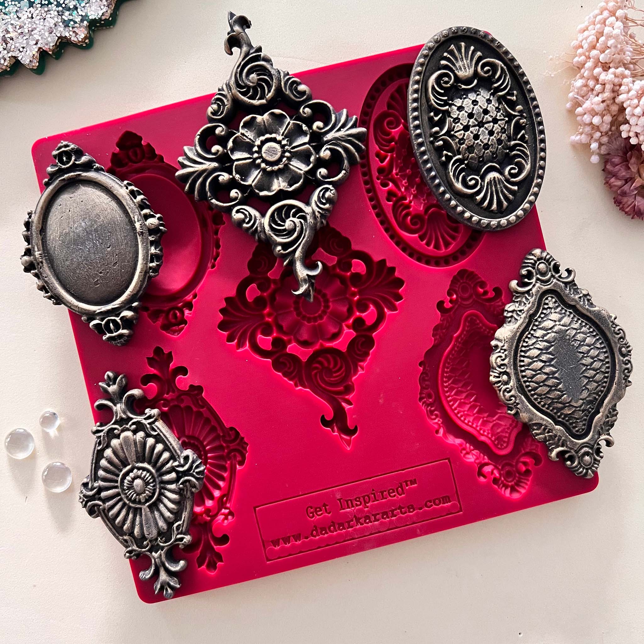 A red silicone mold with 5 dark silver colored castings of vintage medallions are against a light beige background.