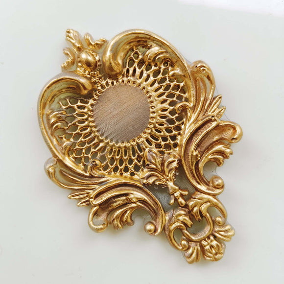 A gold colored casting of a large chandelier style crown medallion is against a white background.