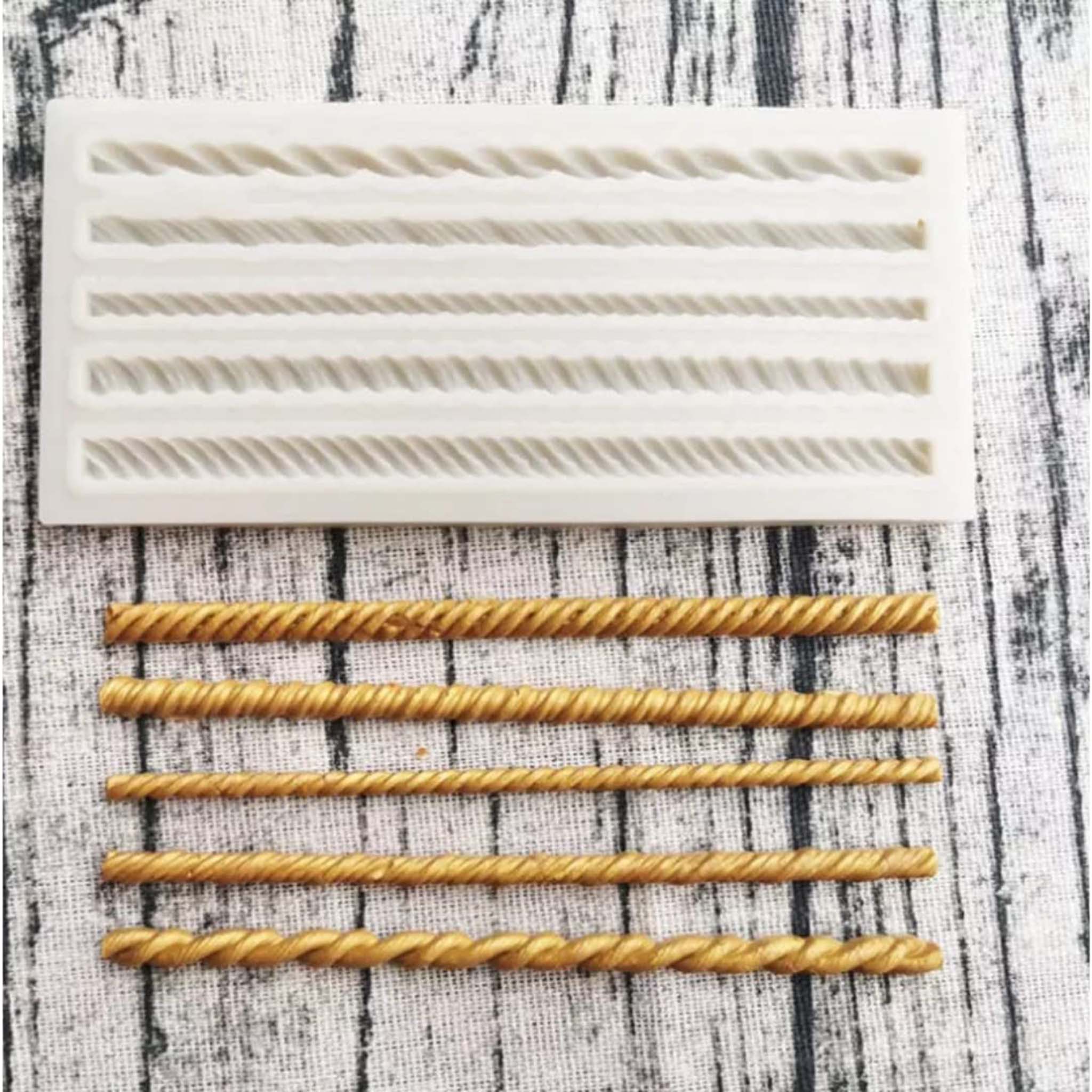 A light beige silicone mold and gold colored castings of 5 mini rope borders are against a grey striped material background.