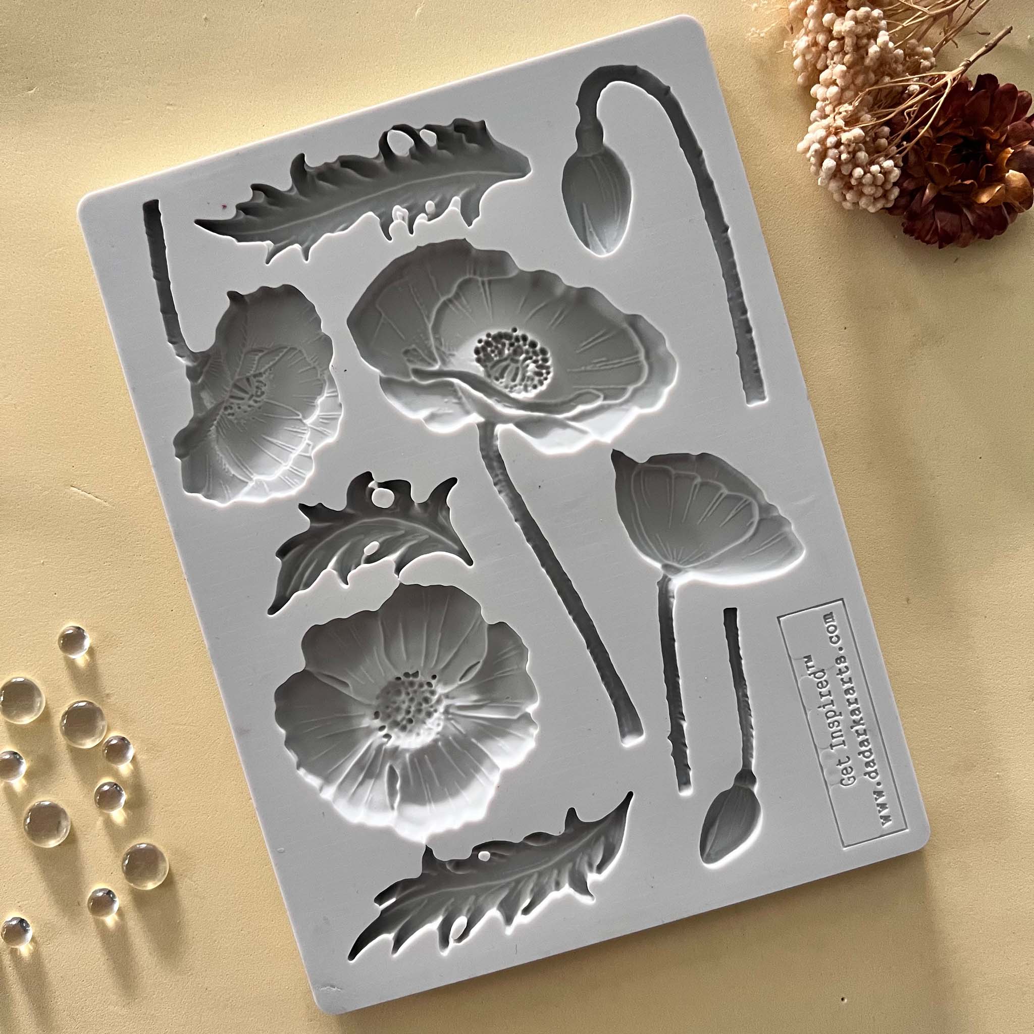 A light grey silicone mold featuring flower blooms, buds, and leaves is against a beige background.