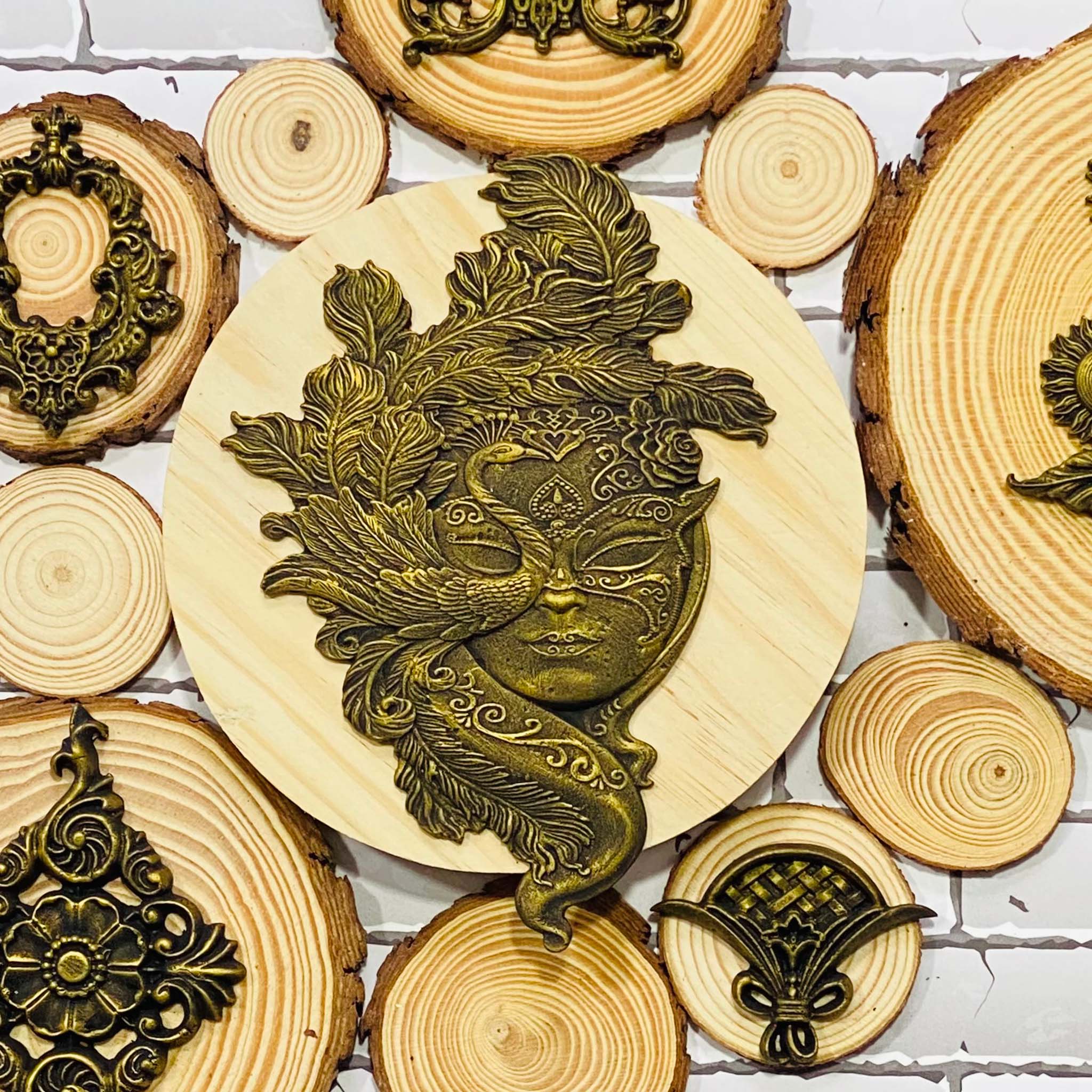 A dark gold colored silicone mold casting of a masquerade mask that features a peacock is on a round piece of wood surrounded by other smaller pieces with wood with more silicone mold castings.