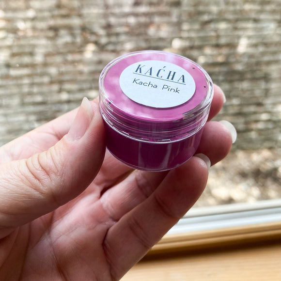 A small 0.5 oz container of a sample of KACHA Pink furniture paint is being held.