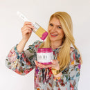 A headshot photo of KACHA holding an open container and paint brush of KACHA Pink Furniture Paint.