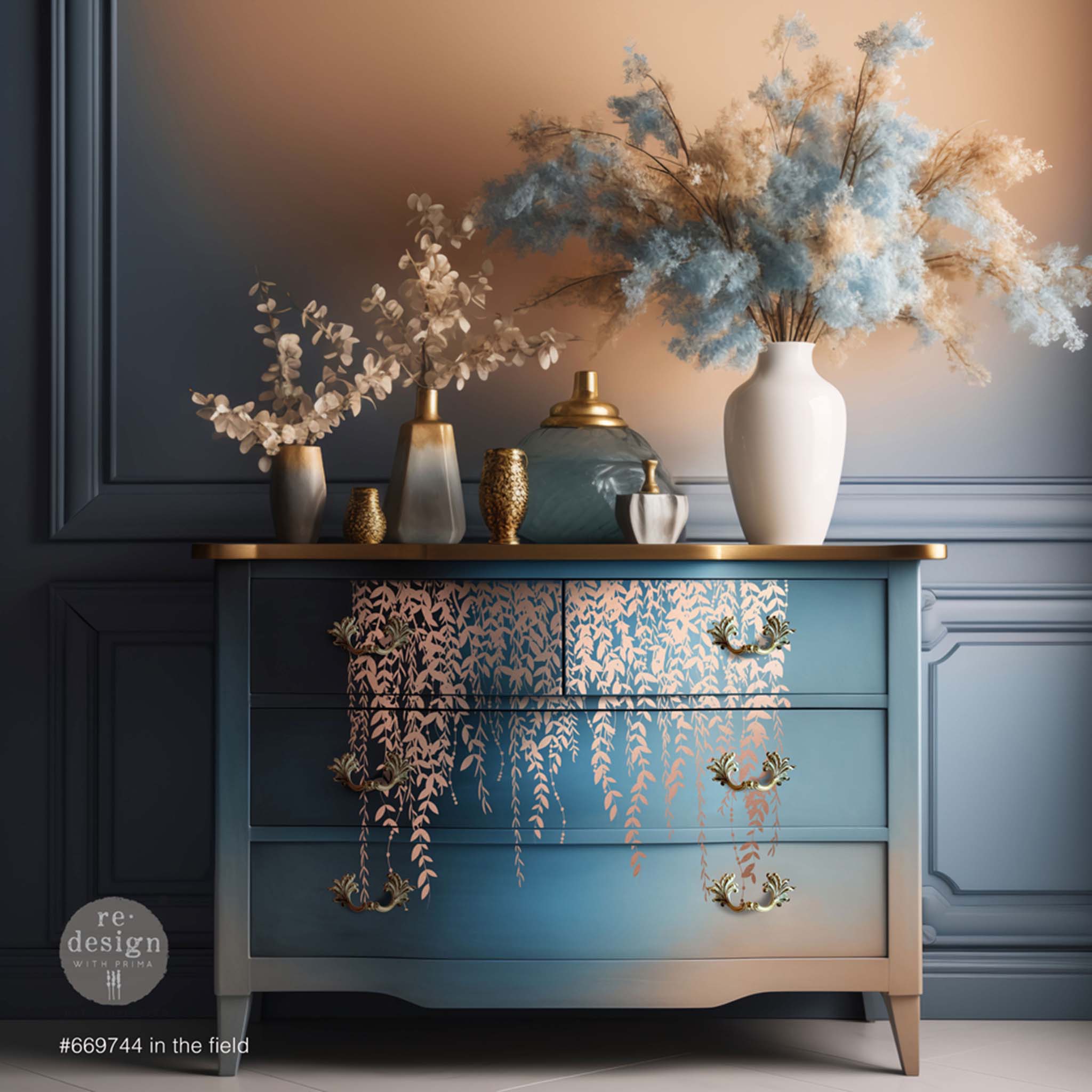 A 4-drawer dresser is painted an ombre of blue down to rose gold and features ReDesign with Prima's Kacha In the Field rose gold foil transfer vining down the center of the drawers.