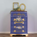 A vintage dresser with a flip-down writing top refurbished by Kacha is painted bue with gold accents and features ReDesign with Prima's Kacha Les Roses on the front of it. 