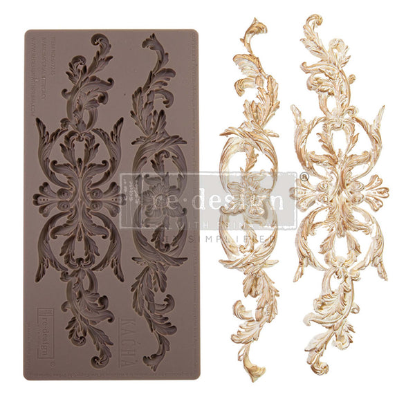 A brown silicone mould and gold/white castings of 2 intricately designed leafy scroll accent pieces are against a white background.