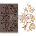 A brown silicone mould and gold/white casting of a large leafy flourish with a central medallion and 2 smaller leafy flourishes are against a white background.