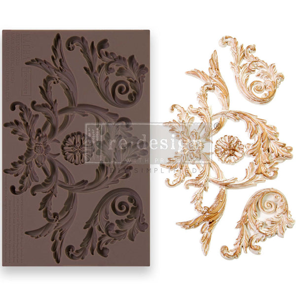 A brown silicone mould and gold/white casting of a large leafy flourish with a central medallion and 2 smaller leafy flourishes are against a white background.