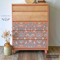 A 5-drawer chest dresser refurbished by Gently Loved Co. is painted coral pink. The top 2 drawers are natural light wood stained and the bottom 3 are painted coral pink and feature ReDesign with Prima's Albery transfer on them.