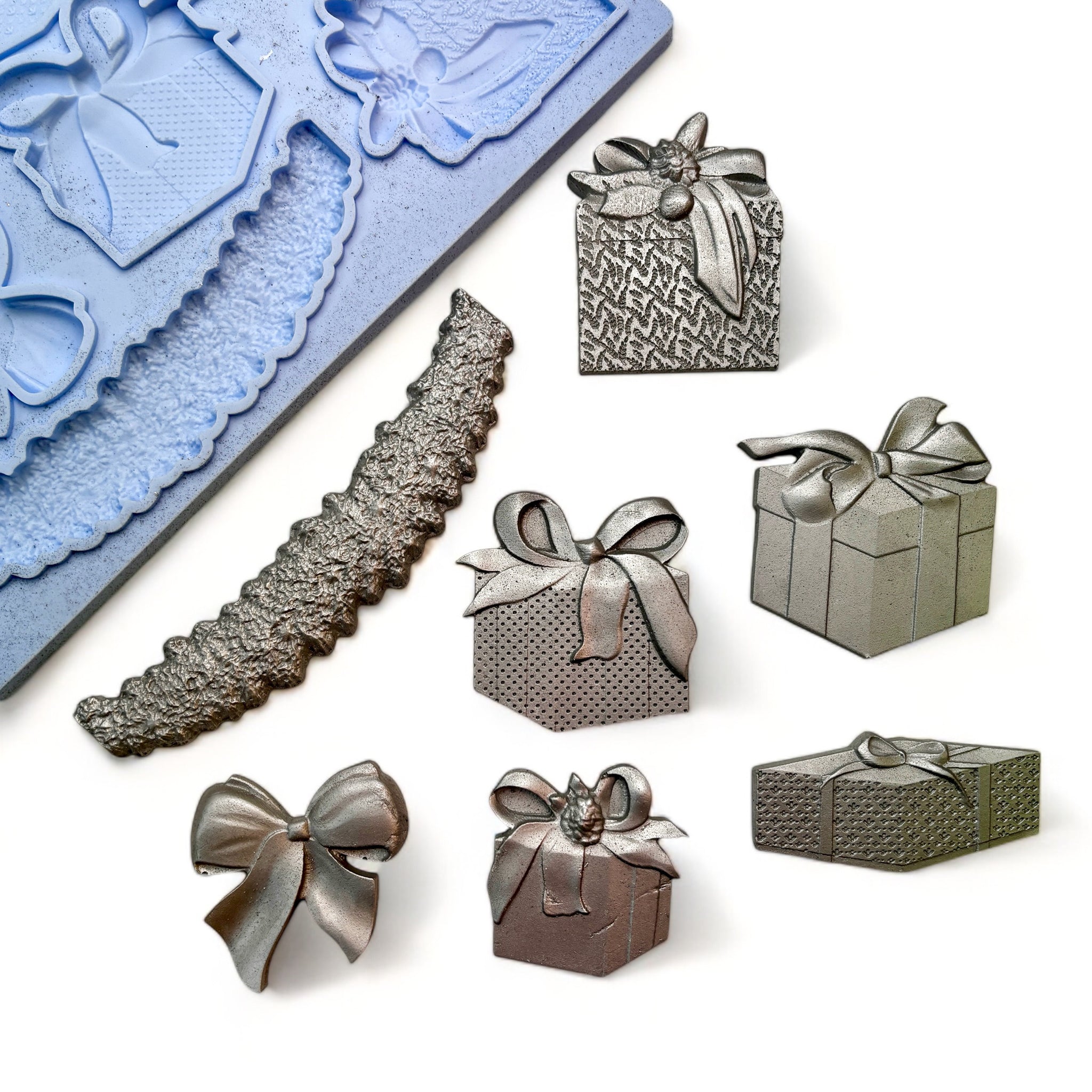 A blue silicone mold and silver colored castings of 5 beautifully wrapped packages, complete with a large bow and garland are against a white background.