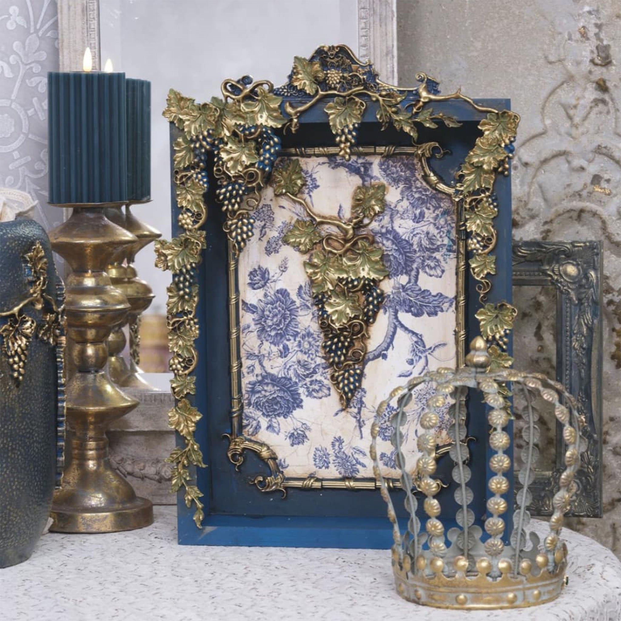 A wood picture frame that is painted blue with a blue toile design features antique silver colored castings of LaBlanche's Grapes silicone mold.