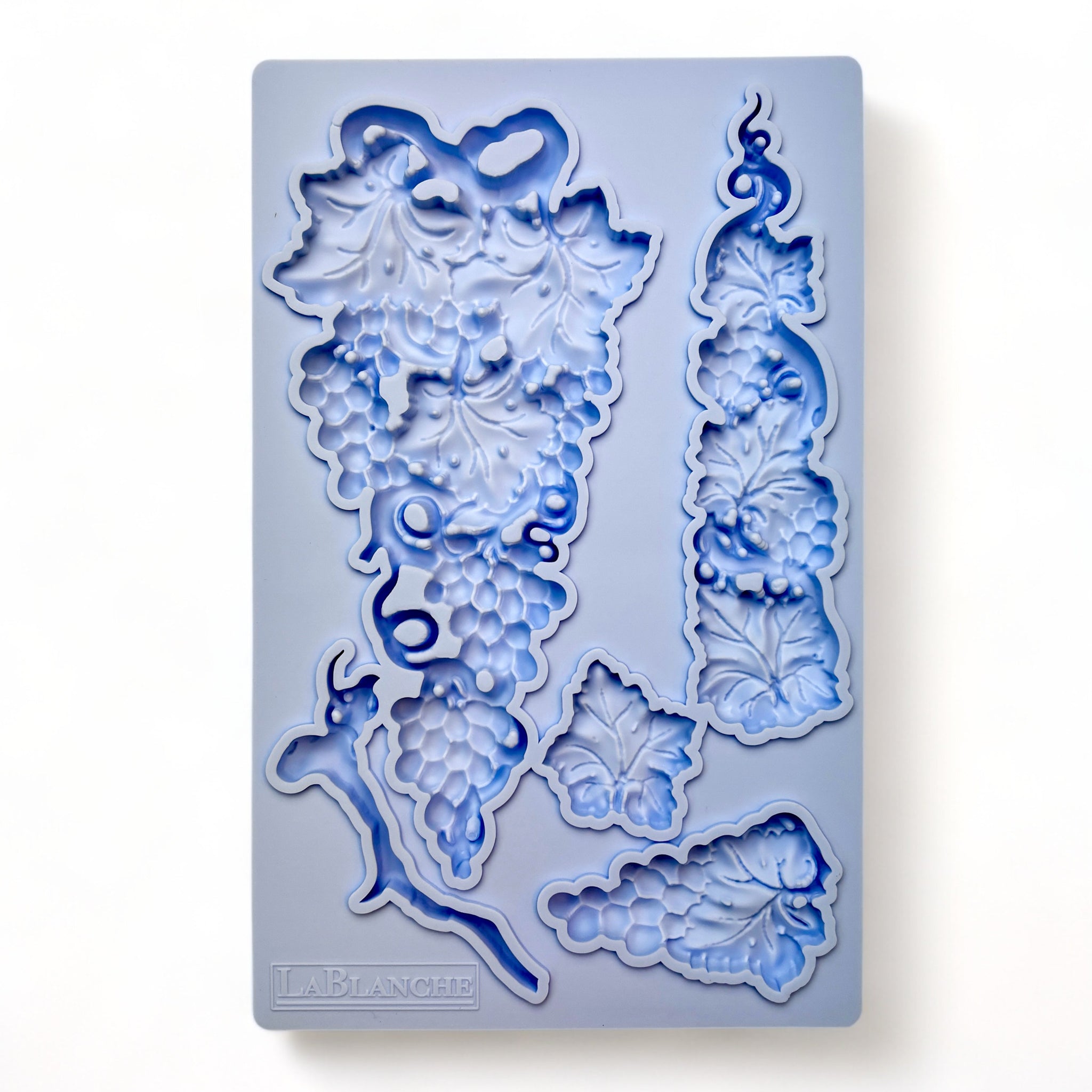 A blue silicone mold of 3 clusters of grapes, a loose leaf, and a branch is  against a white background.