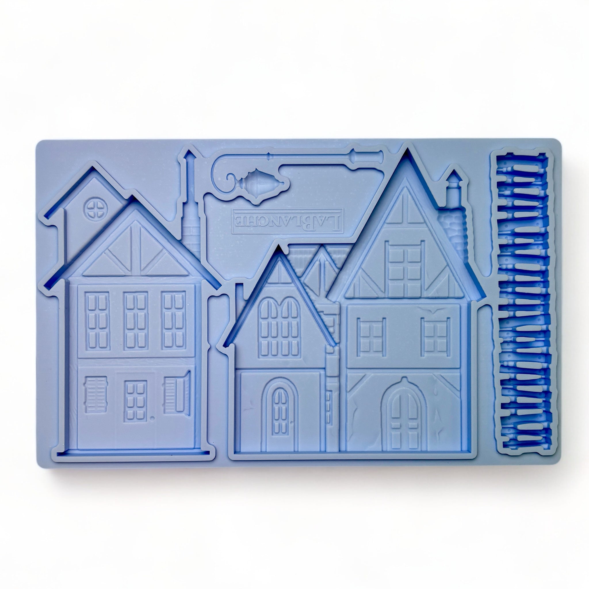 A blue silicone mold of 2 homes, a picket fence, and a lamp post is against a white background.