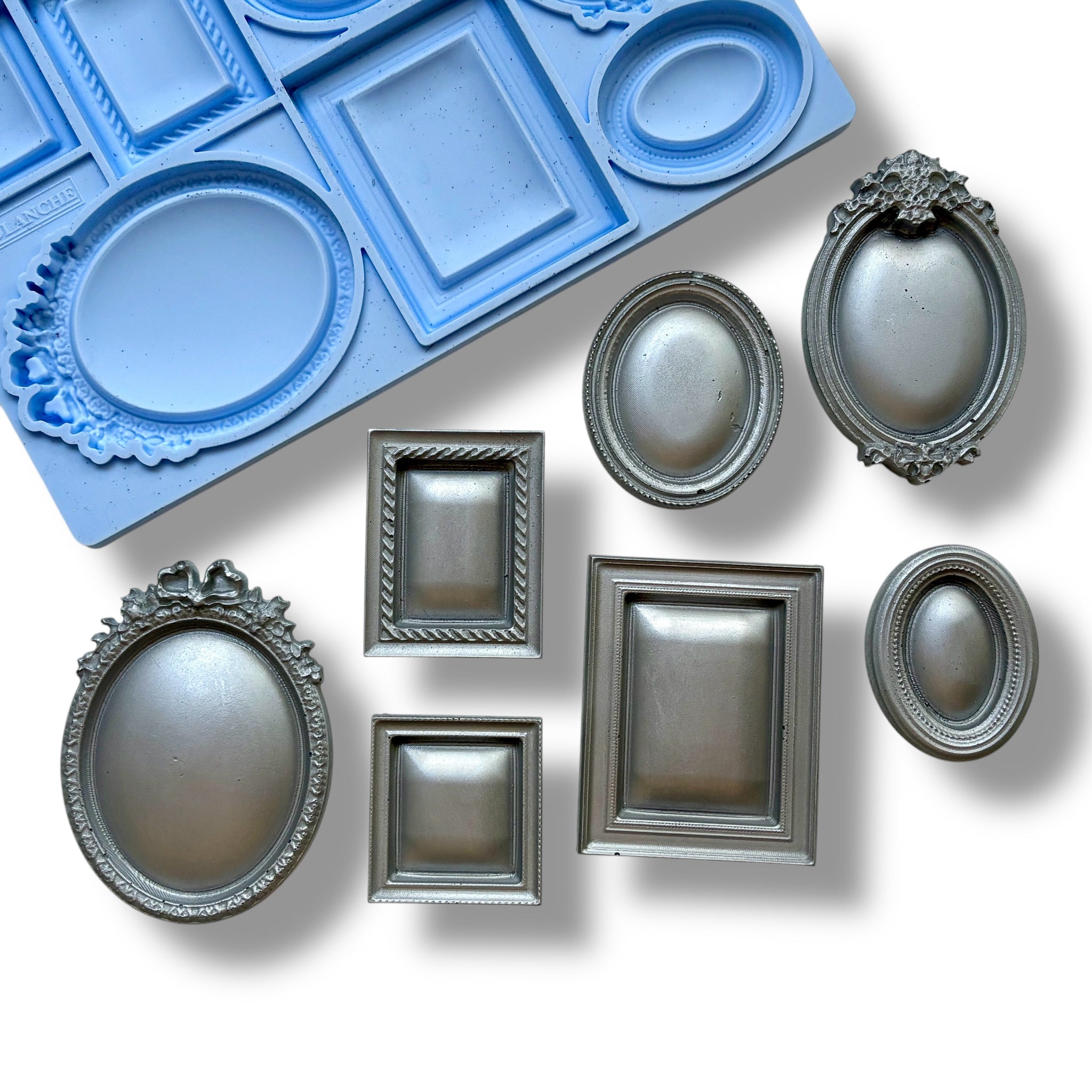 A blue silicone mold and silver colored castings featuring 7 small square, oval, and rectangular vintage photo frames are against a white background.