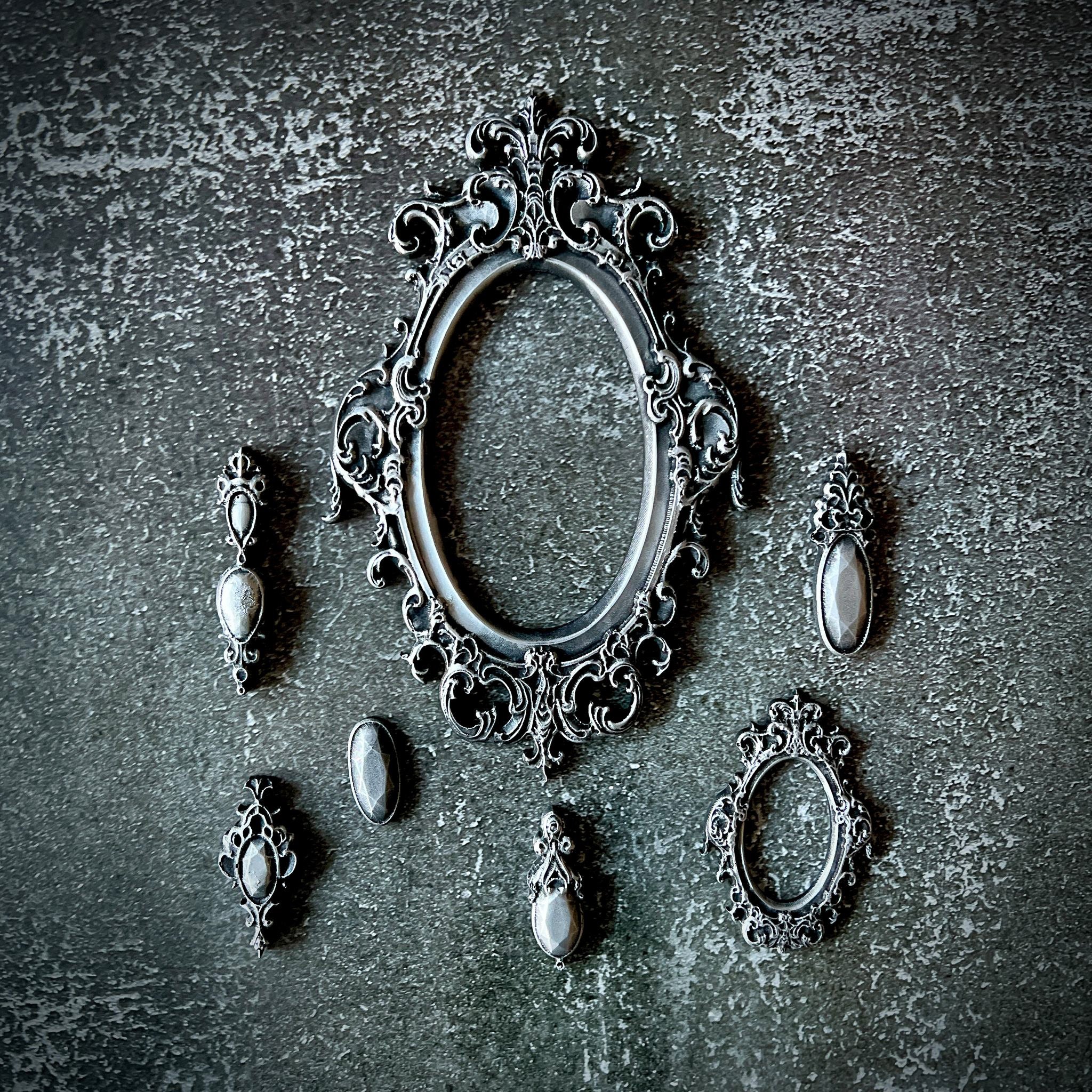 Silver silicone mould castings of 2 ornate oval frames and 5 ornate pendants are against a grey textured background.