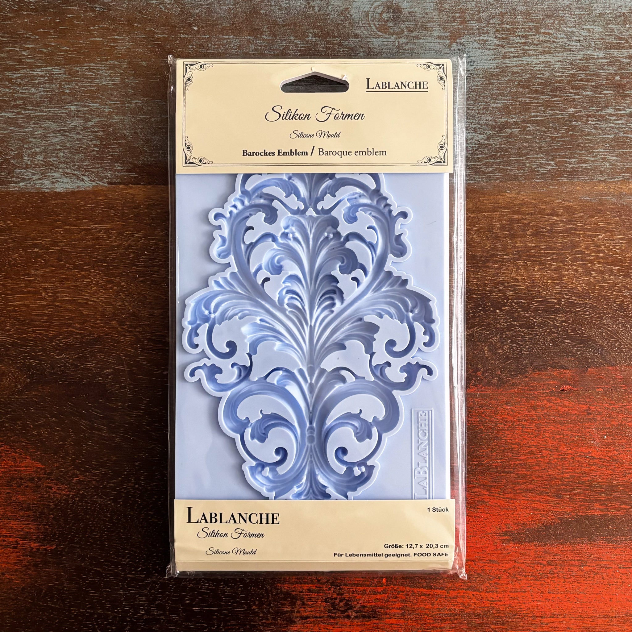 A package of LaBlanche's Baroque Emblem silicone mold is against a dark wood background.