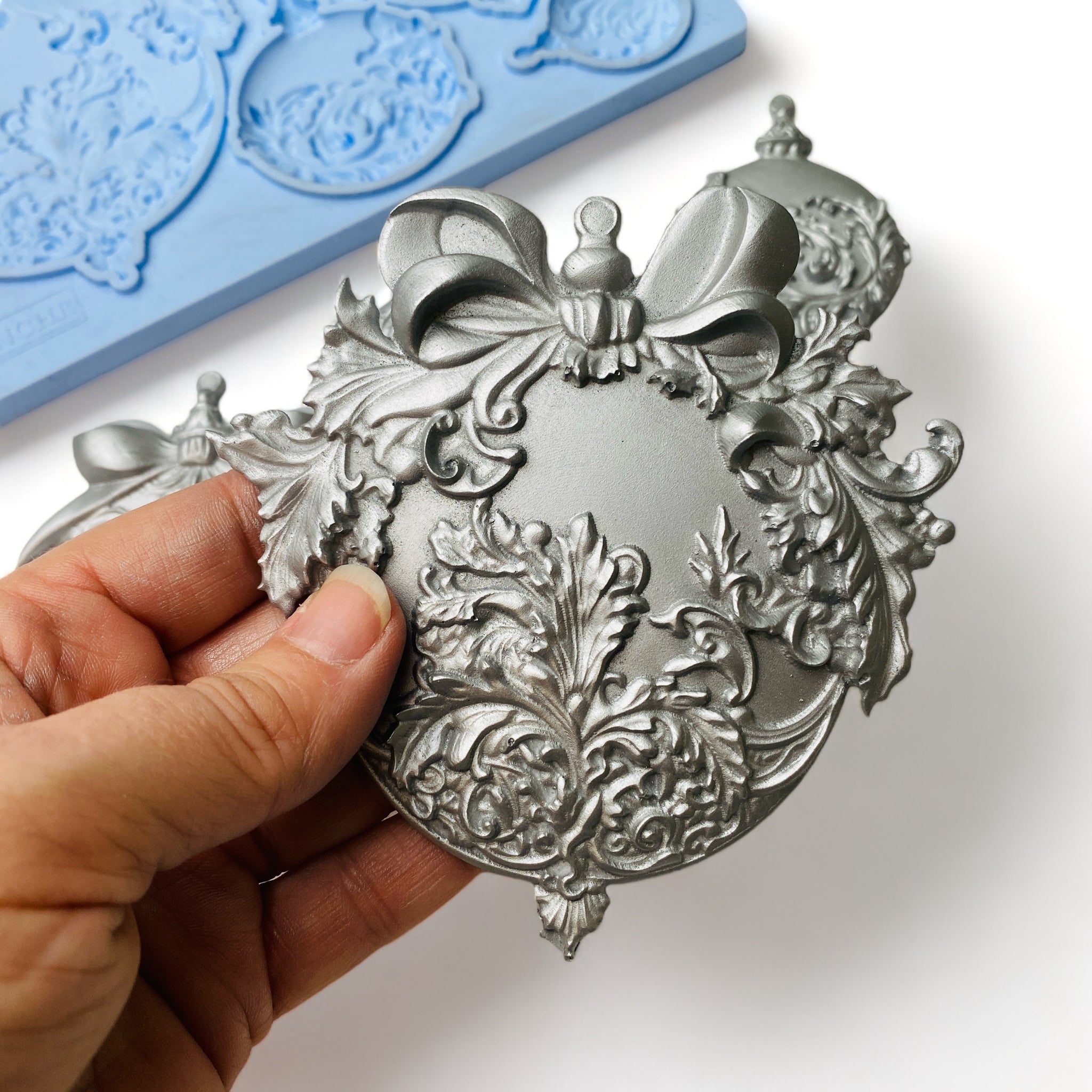 A hand is shown holding a silver colored casting made from LaBlanche's Christmas Balls silicone mold.