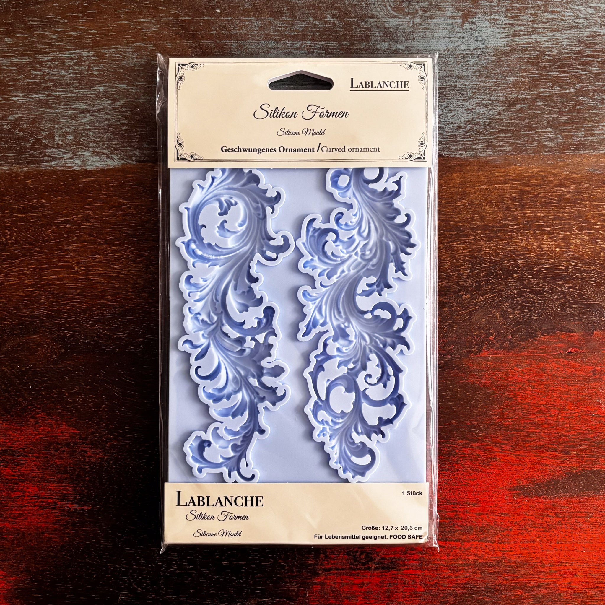 A package of LaBlanche's Curved Ornament silicone mold is against a dark wood background.