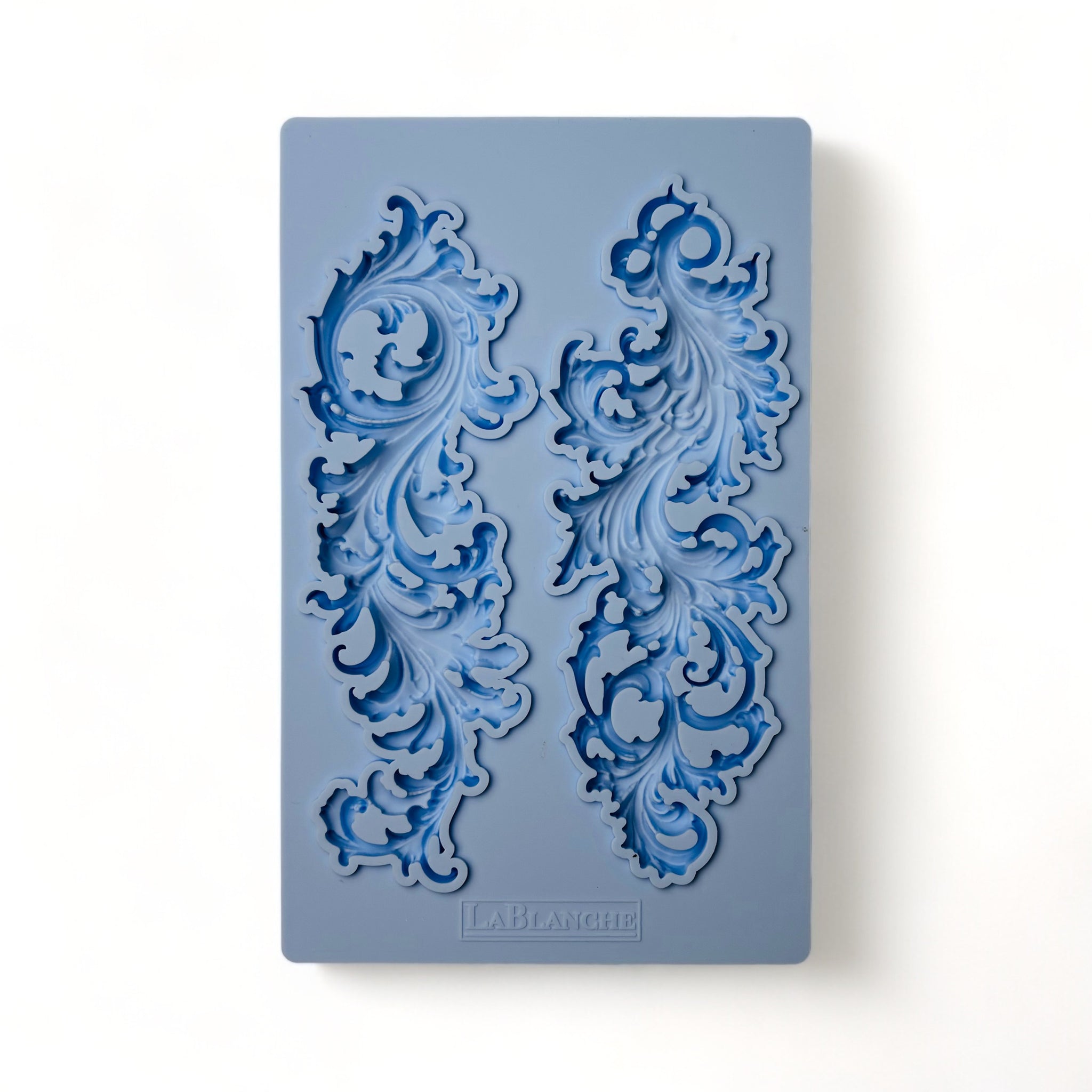 A blue silicone mold of 2 leafy flourishes is against a white background.