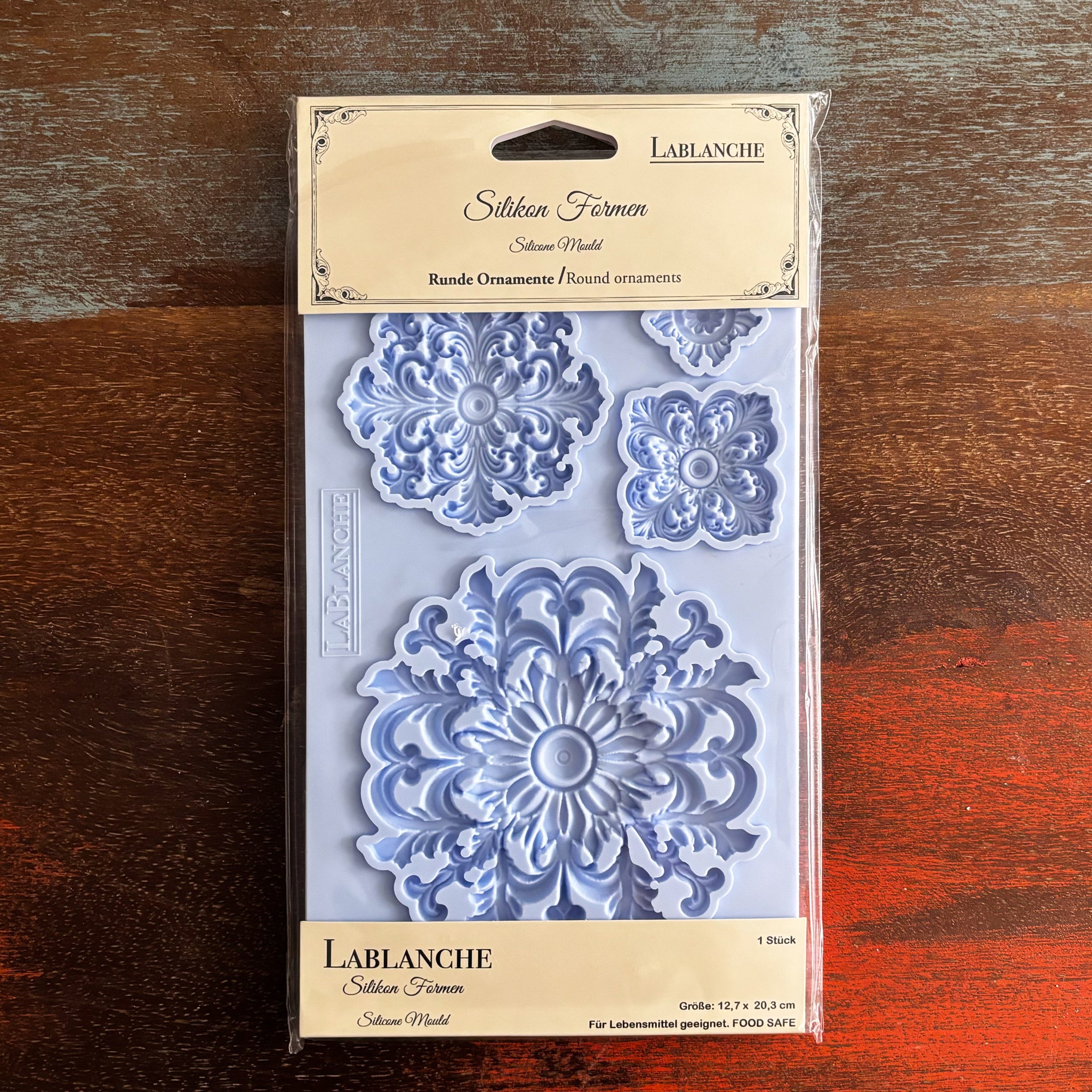 A package of LaBlanche's Round Ornament silicone mold is against a dark wood background.