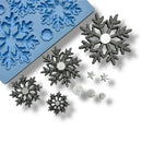 Metal snowflakes on a white background next to a blue silicone mold.