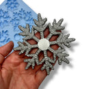 Silver snowflake-shaped mold held in a hand with a blue silicone mat in the background