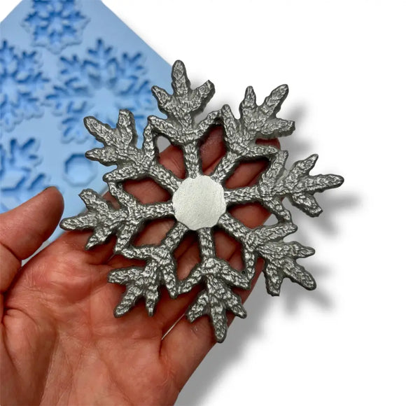 Silver snowflake-shaped mold held in a hand with a blue silicone mat in the background