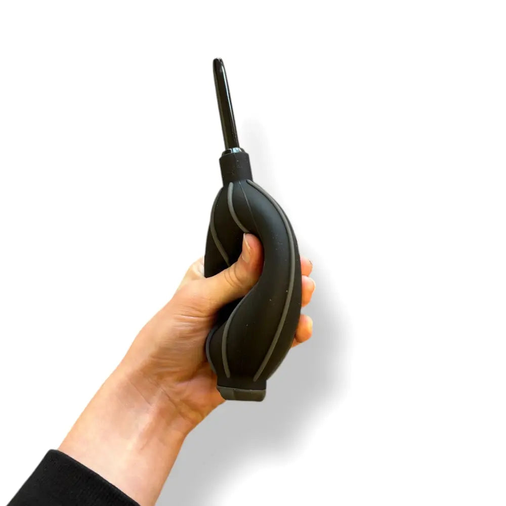 A hand is shown squeezing a black large air puffer against a white background.