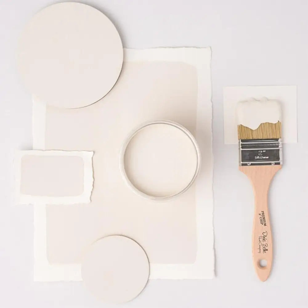 A paint brush, paper, and round wood samples of Dixie Belle's Magnolia Chalk Mineral Paint are against a white background.