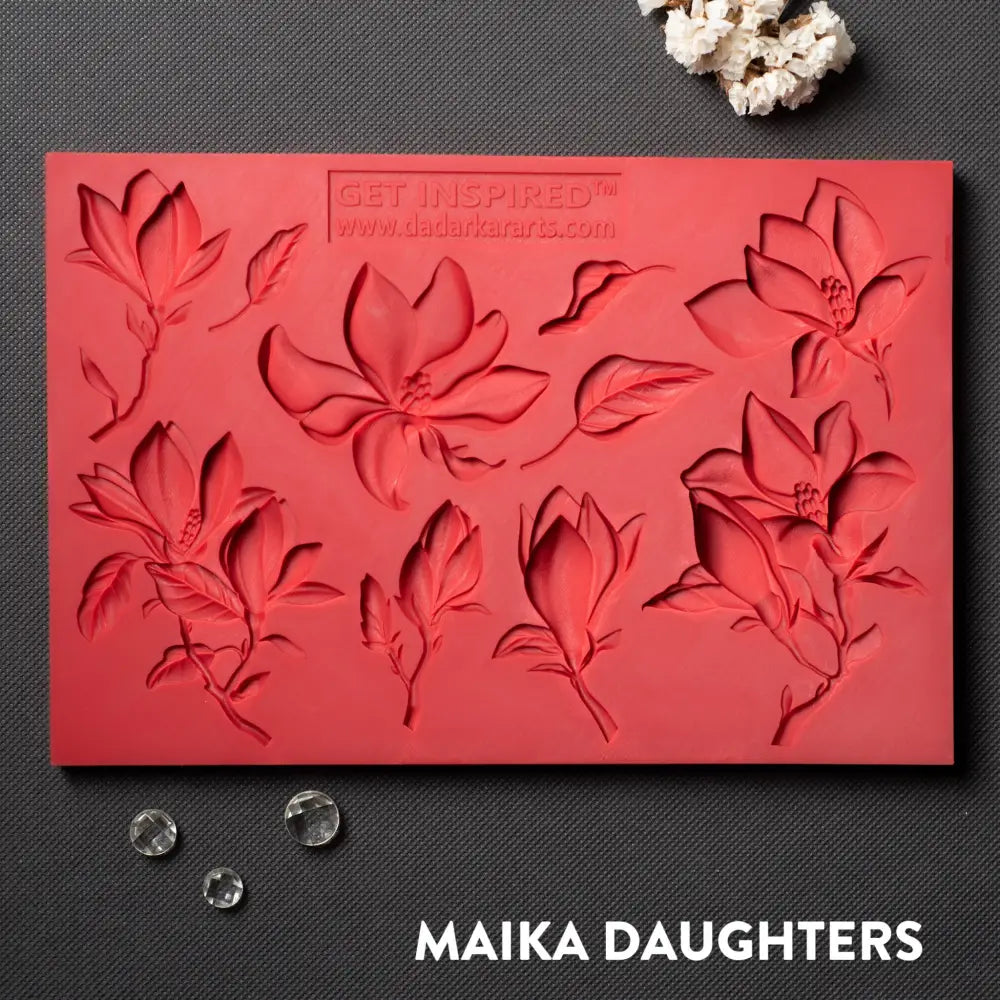 A red silicone mold featuring 8 magnolia flower blooms and 2 leaves is against a dark grey material background. 