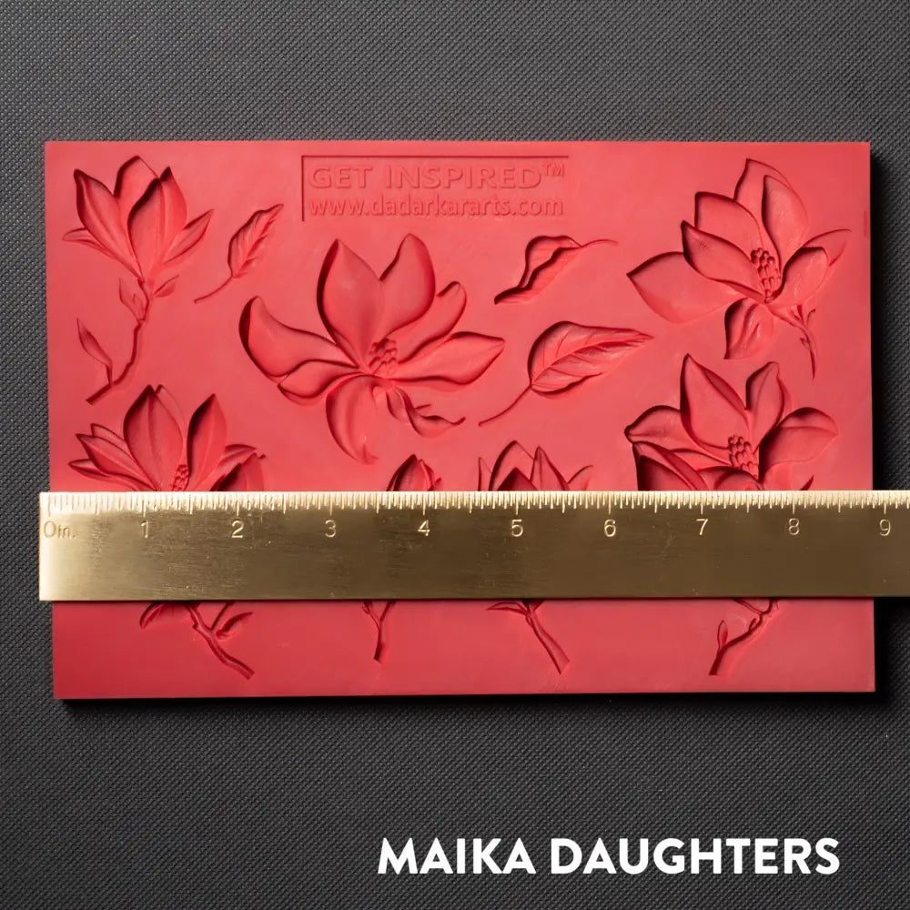 A red silicone mold featuring 8 magnolia flower blooms and 2 leaves is against a dark grey material background. A gold ruler reading 9" length sits on the mold.