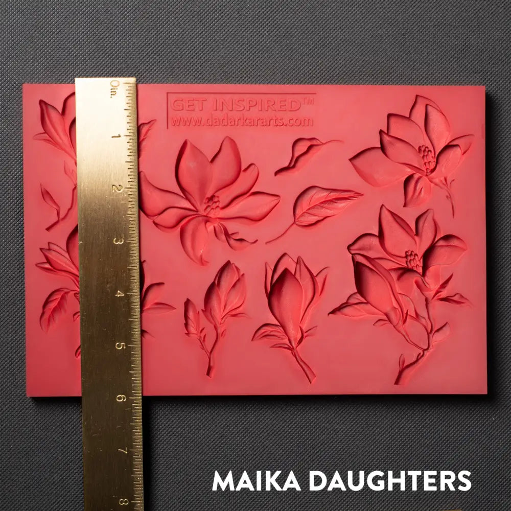 A red silicone mold featuring 8 magnolia flower blooms and 2 leaves is against a dark grey material background. A gold ruler reading 6" height sits on the mold.