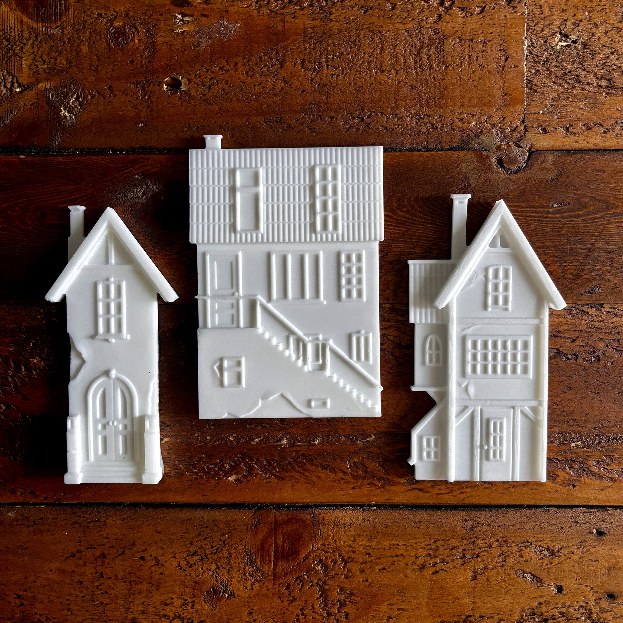 White resin silicone mold castings of 3 houses are against a dark wood background.