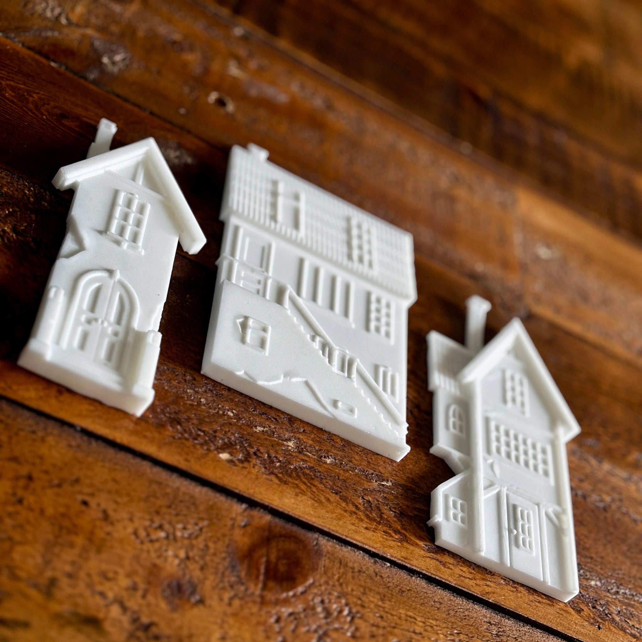 White resin silicone mold castings of 3 houses are against a dark wood background.