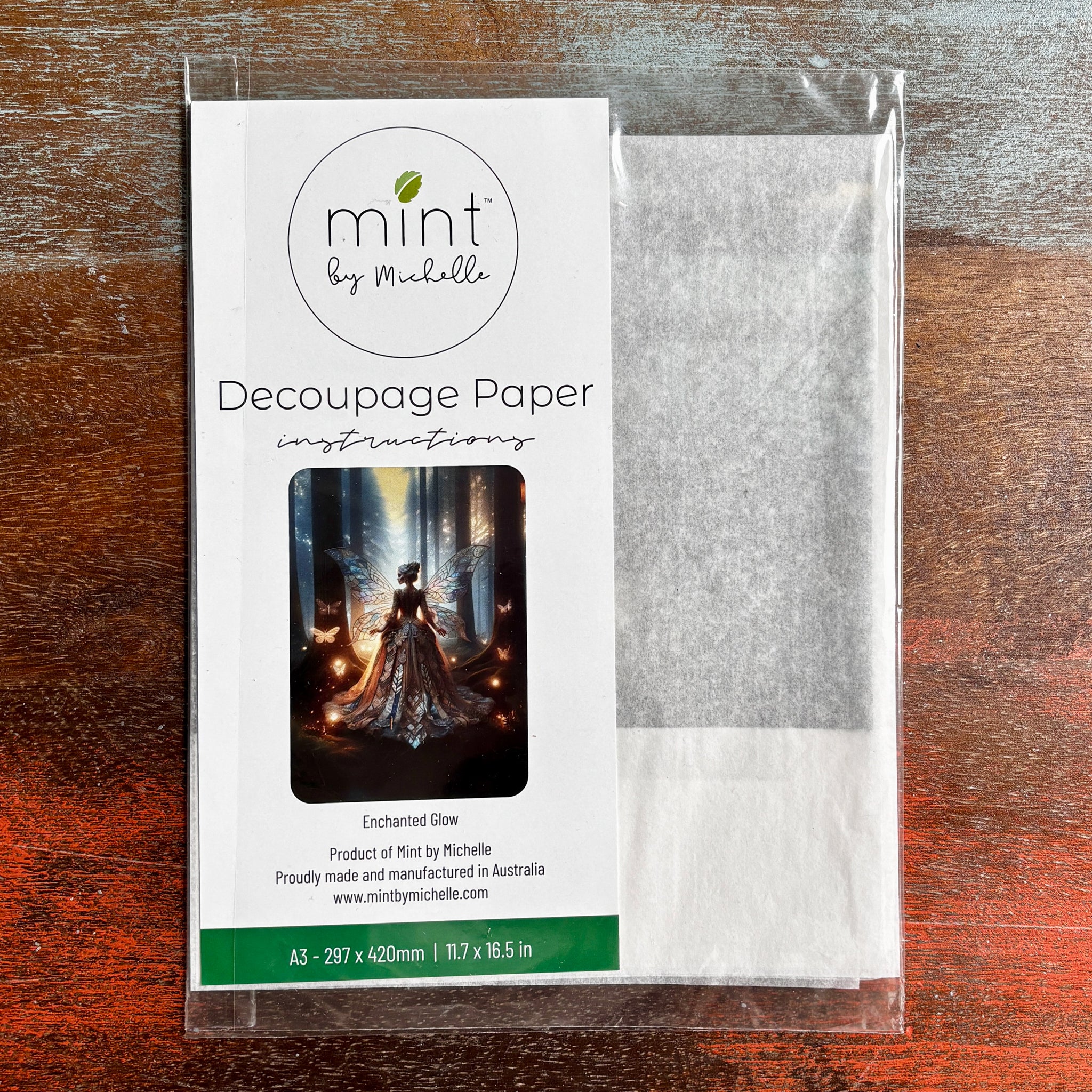 A package of Mint by Michelle’s Enchanted Glow A3 Decoupage Paper is against a dark wood background. 
