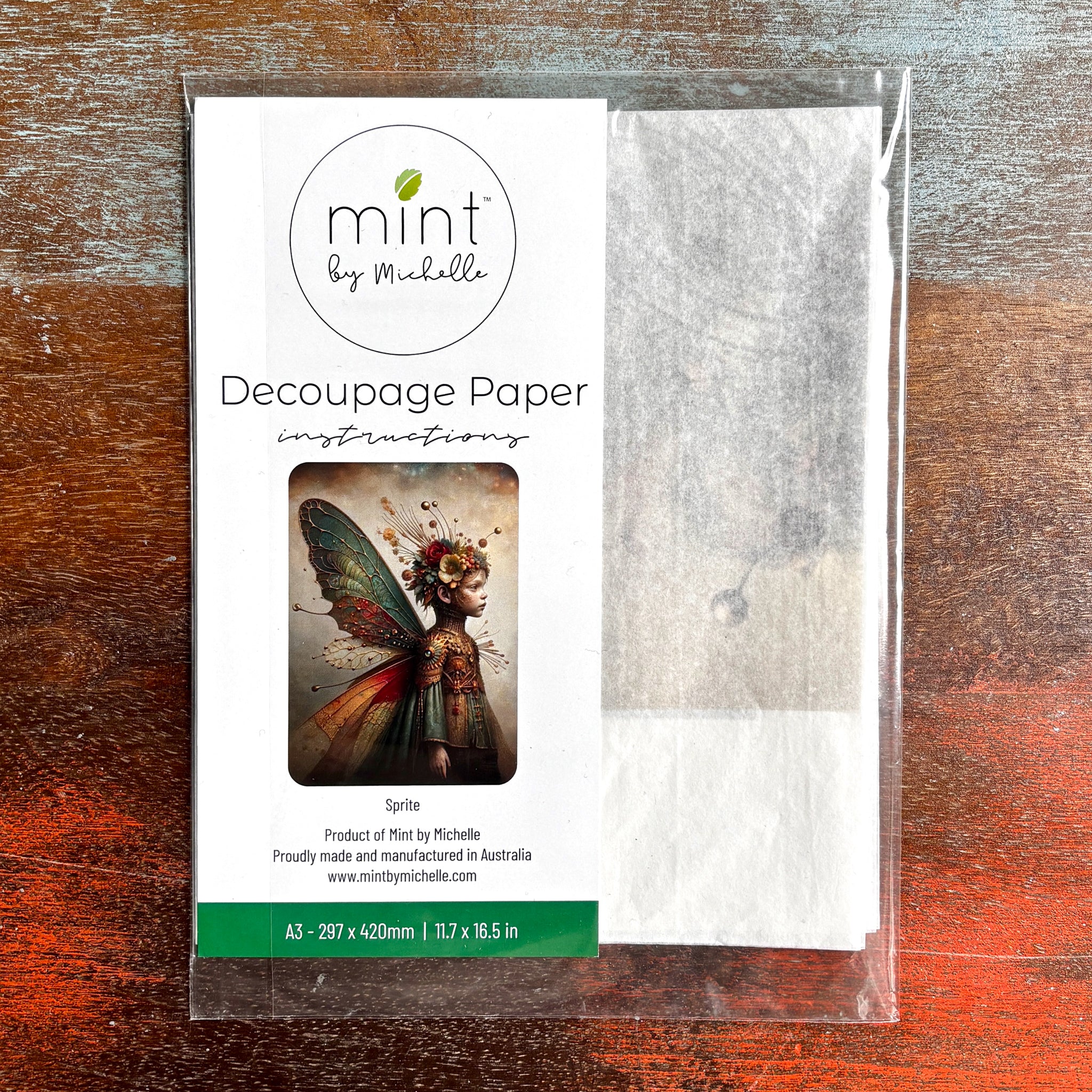 A package of Mint by Michelle’s Sprite A3 Decoupage Paper is against a dark wood background. 
