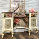 Decorative cabinet with floral design and gold accents against a brick wall.