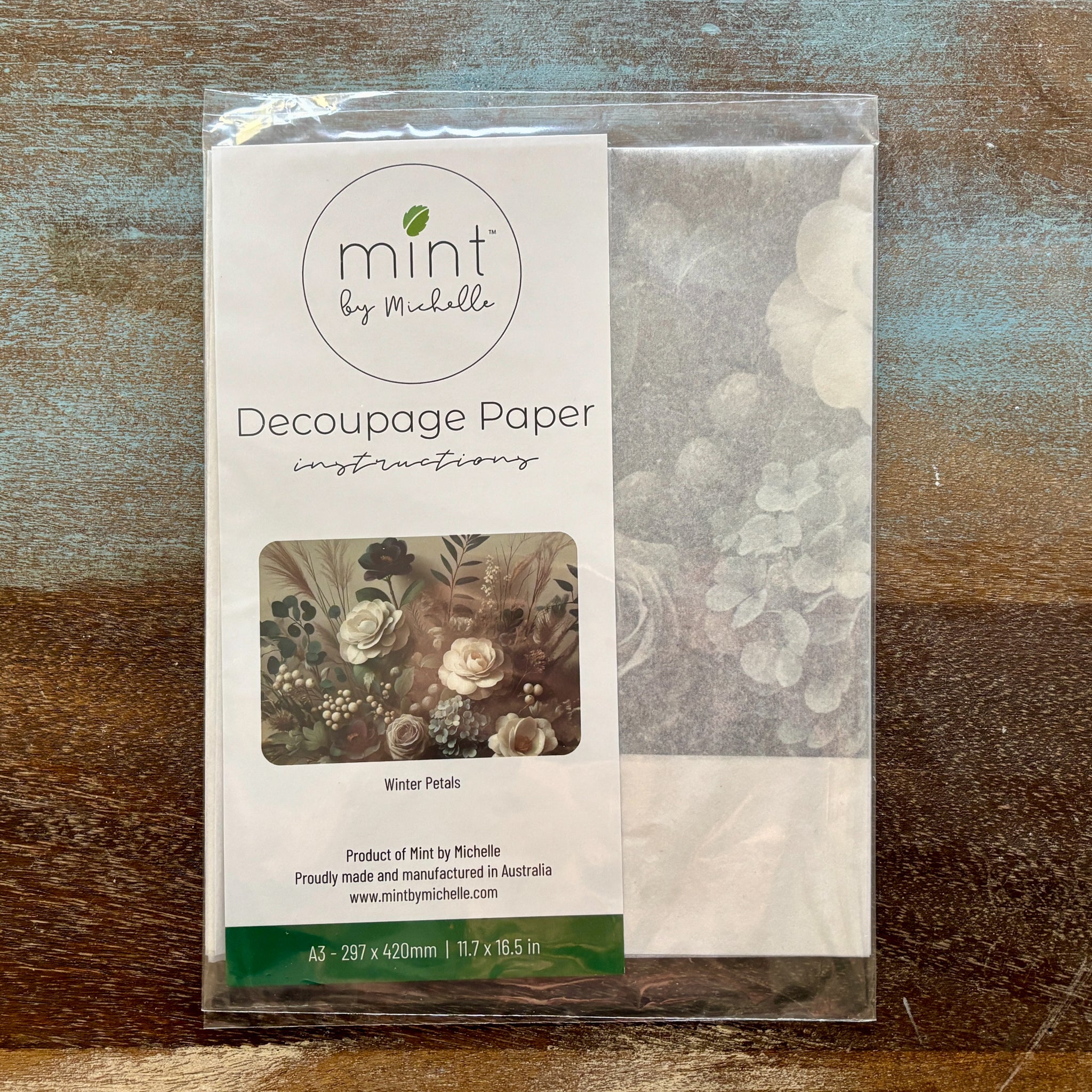 A package of Mint by Michelle's Winter Petals A3 Decoupage Paper is against a wood background.