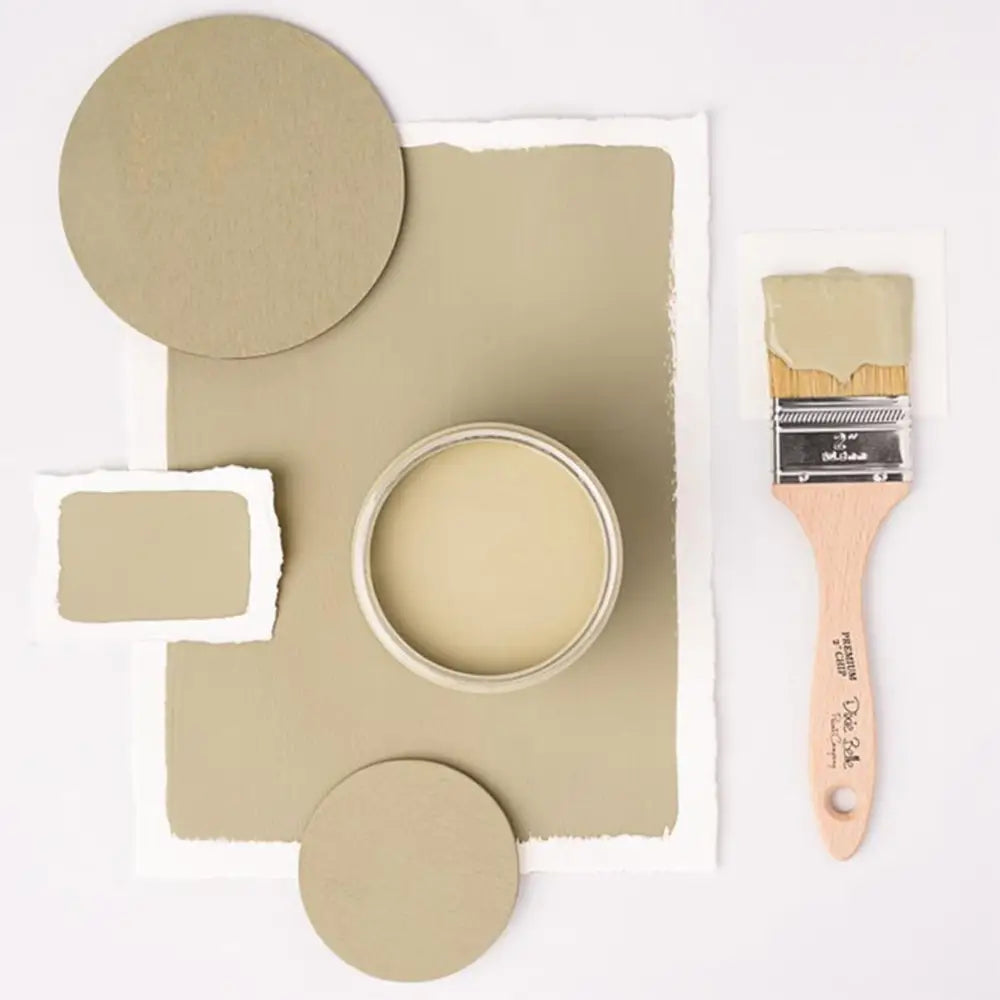 A paint brush, paper, and round wood samples of Dixie Belle's Olive Wood Chalk Mineral Paint are against a white background.