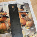 Halloween-themed paper with pumpkins and a cat, ruler for scale, on a textured surface.