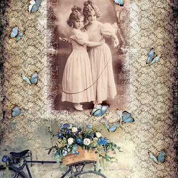 Close-up of a rice paper featuring a collage of a sepia vintage portrait of two young girls in an embrace against a background of a patterned design with blue butterflies and bicycle with blue flowers in a basket.
