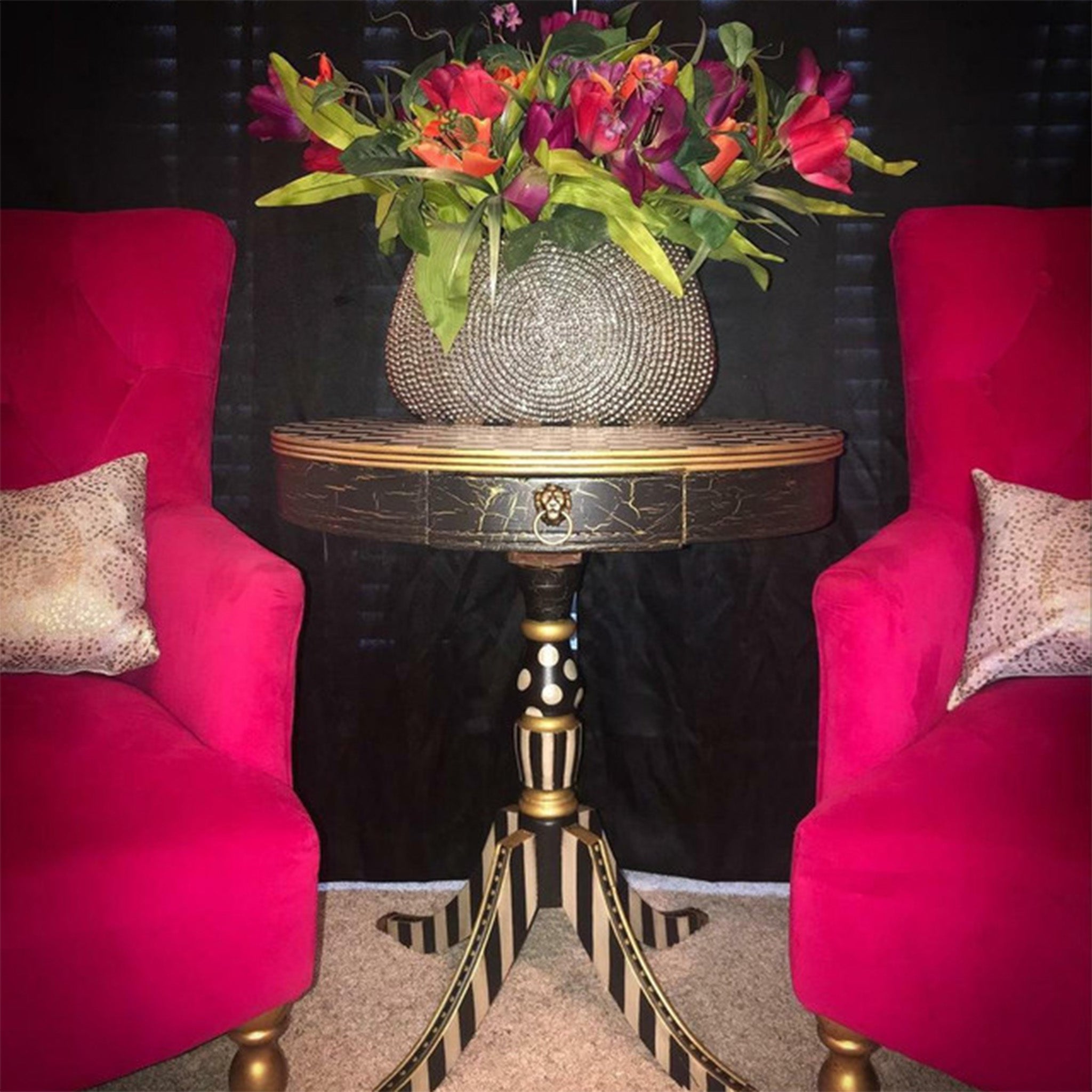 A vintage side table between 2 red chairs features Pentart's Fine Line Crackle painted black on it. A colorful bouquet of flowers in a rhinestone planter sits on the table.