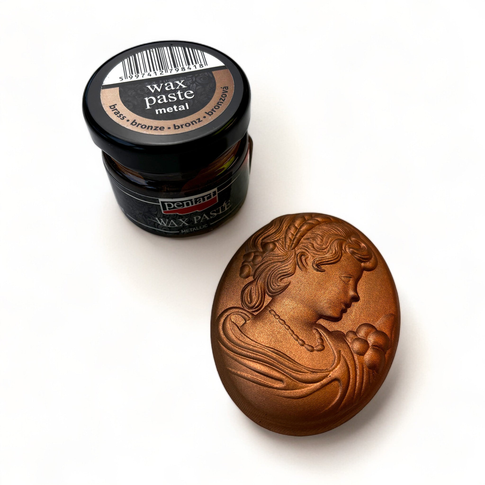 A jar of Pentart's Bronze Metallic Wax Paste and a silicone mold casting of a cameo pendant finished in the wax are against a white background.