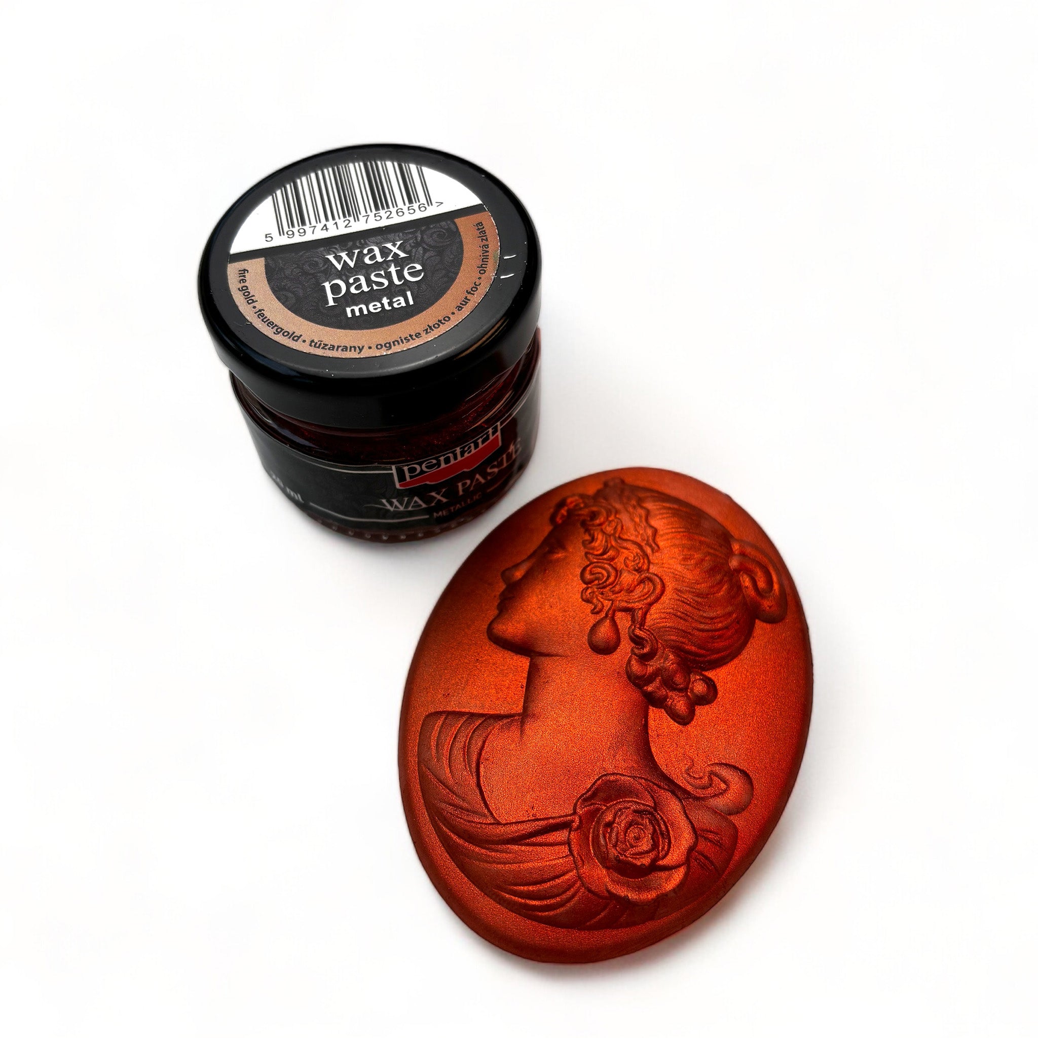 A jar of Pentart's Fire Gold Metallic Wax Paste and a silicone mold casting of a cameo pendant finished in the wax are against a white background.